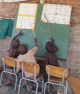 Afrikanische Schulkinder deuten mit Stöcken auf eine Silbentabelle zum Lesenlernen